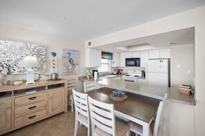 A compact kitchen with white cabinetry, a central island, and a dining area with white chairs. - Sunswept 408 by Liquid Life (Orange Beach)