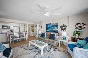 A modern living room with a dining area, kitchen, and a ceiling fan. - Sunswept 408 by Liquid Life (Orange Beach)