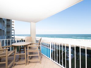 A balcony with a view of the beach and ocean, wooden furniture, and a pool area. - Sunswept 408 by Liquid Life (Orange Beach)