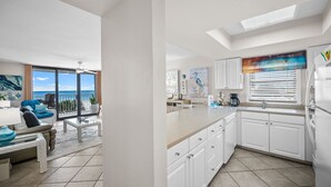 Uma cozinha moderna com armários brancos, uma ilha grande e vista para o oceano pelas portas de correr de vidro.