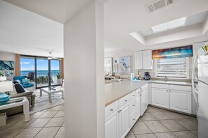 A modern kitchen with white cabinets, a large island, and a view of the ocean through the sliding glass doors. - Sunswept 408 by Liquid Life (Orange Beach)