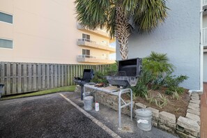 Ein Grillplatz im Freien mit Grill und Tisch, einem Holzzaun und einem Gebäude im Hintergrund.
