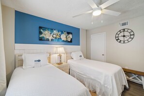 Habitación de hotel con dos camas, ventilador de techo, reloj de pared y una obra de arte con forma de estrella de mar.