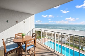 Un balcon avec une table et des chaises, donnant sur une piscine et une plage.