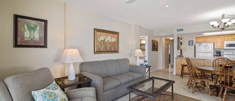 A living room with a gray sofa, a coffee table, and a patterned rug. There is a ceiling fan and a chandelier in the living area.