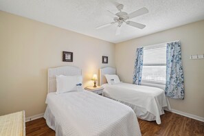A hotel room with two beds, a ceiling fan, a window with floral curtains, and a wall-mounted nightstand with a lamp. - Sunswept 601 by Liquid Life (Orange Beach)