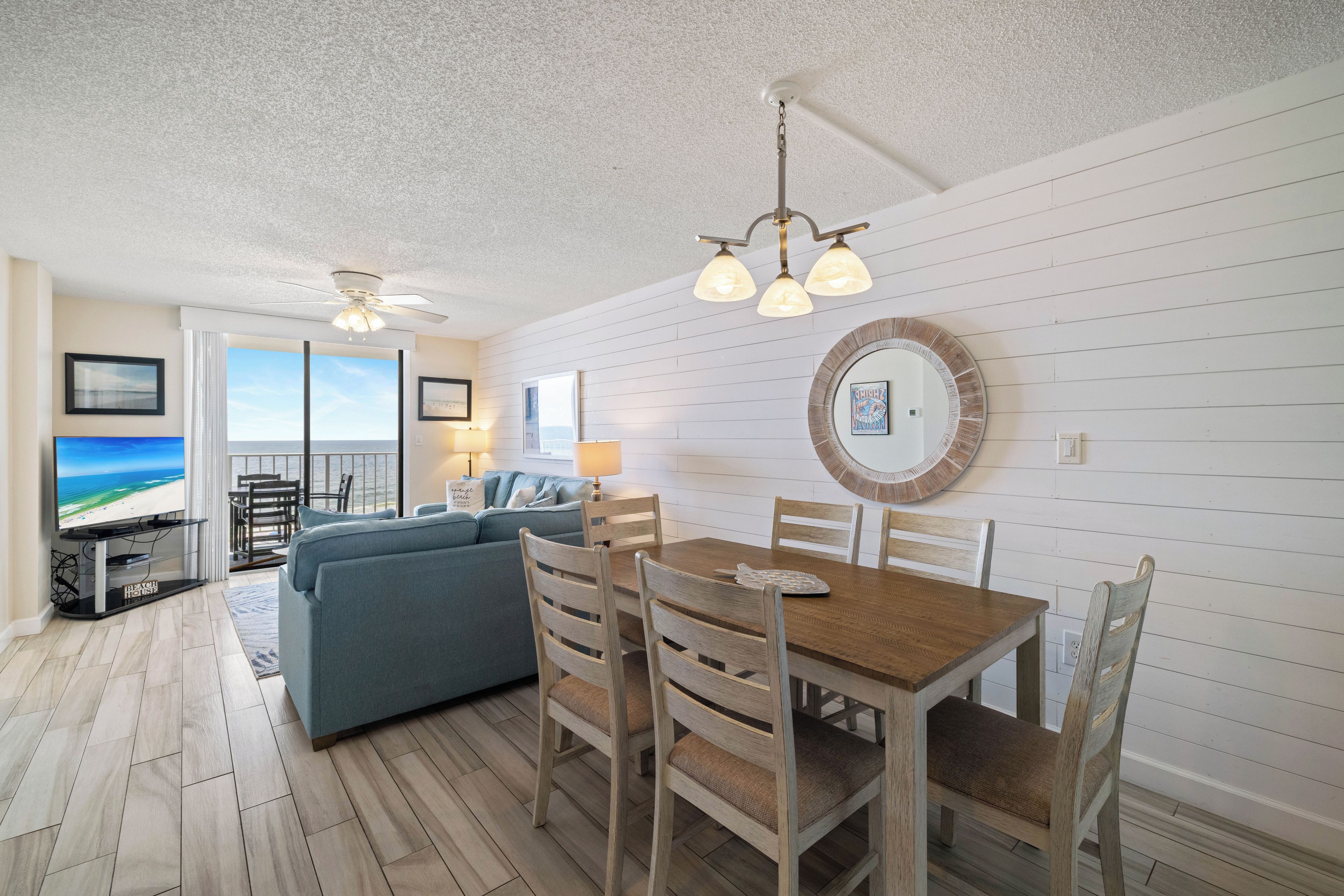 A living room with a sofa, dining table, chairs, a TV, and a view of the ocean.