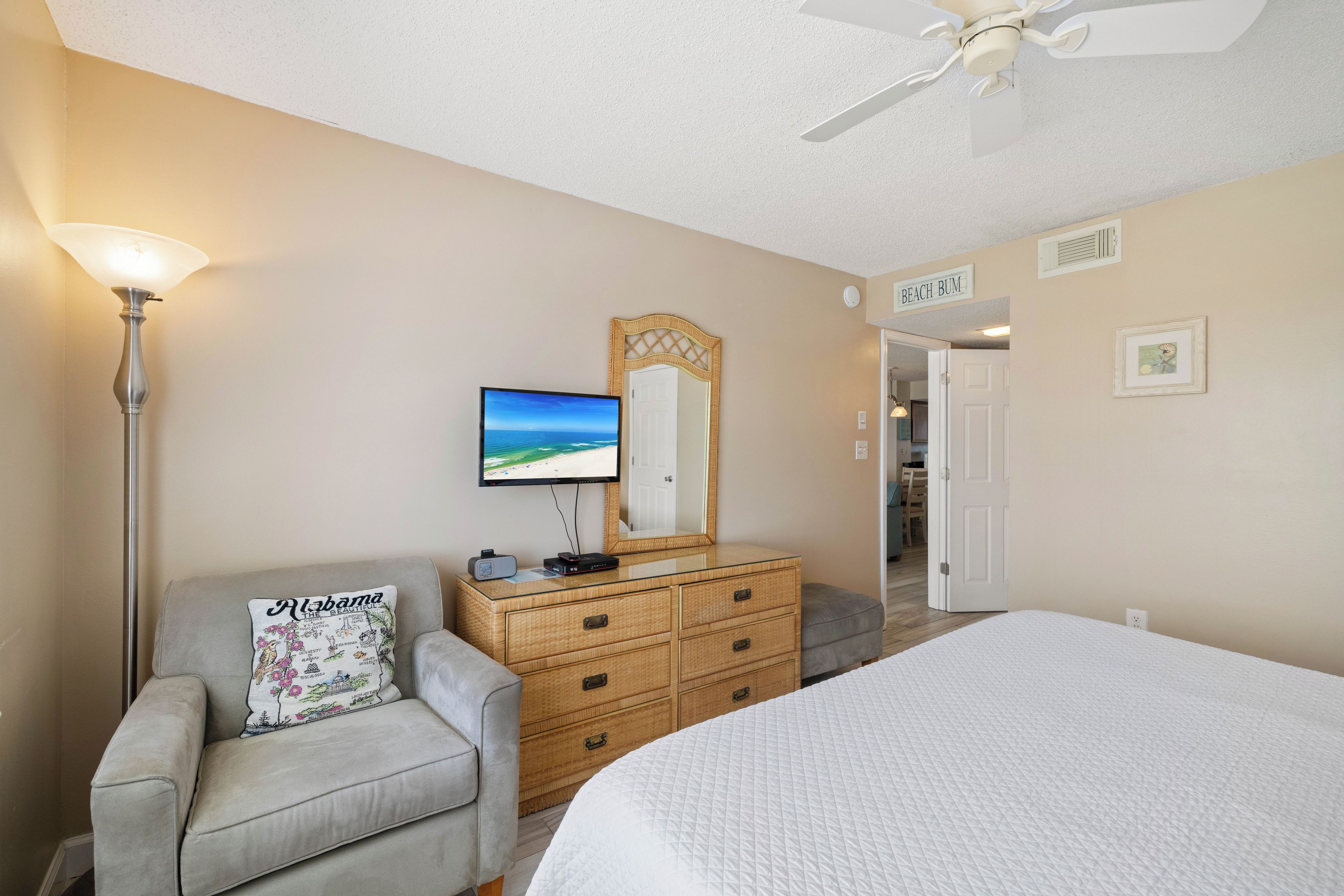 A bedroom with a bed, a television, a dresser, a chair, and a ceiling fan.