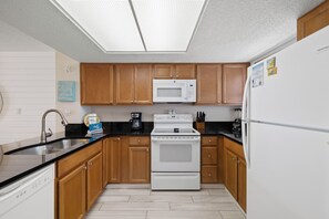 A kitchen with wooden cabinets, a white refrigerator, a microwave, a stove, and a coffee maker. - Sunswept 602 by Liquid Life (Orange Beach)