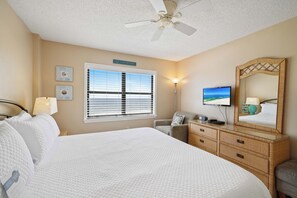 A hotel room with a bed, a desk, a chair, a television, a mirror, and a window with blinds. - Sunswept 602 by Liquid Life (Orange Beach)