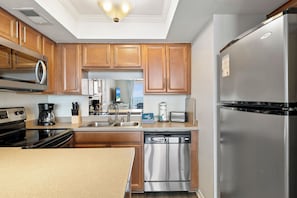 A modern kitchen with stainless steel appliances, wooden cabinets, and a built-in dishwasher. - Sunswept 604 by Liquid Life (Orange Beach)