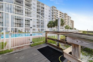 Un bâtiment moderne à plusieurs étages, doté d’un espace piscine comprenant une terrasse en bois et une clôture en métal.