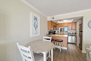 A modern kitchen with wooden cabinets, stainless steel appliances, and a dining area with a white table and chairs. - Sunswept 604 by Liquid Life (Orange Beach)