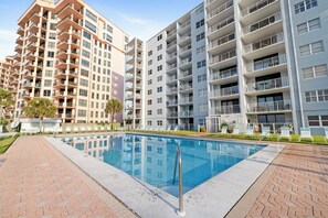 A modern apartment building with a swimming pool, multiple balconies, and a brick pathway. - Sunswept 604 by Liquid Life (Orange Beach)