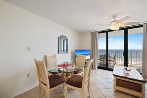 Ein Zimmer mit Balkon, einem Esstisch mit Stühlen, einem Fernseher und Blick auf den Strand.