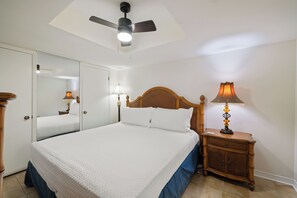 Ein Schlafzimmer mit einem Bett, einem Nachttisch, einer Lampe, einem Deckenventilator und einem Spiegel.