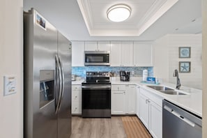A modern kitchen with stainless steel appliances, white cabinetry, and a tiled backsplash. - Sunswept 607 by Liquid Life (Orange Beach)