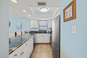 A modern kitchen with white cabinets, a stainless steel refrigerator, and a marble countertop. - Sunswept 608 by Liquid Life (Orange Beach)