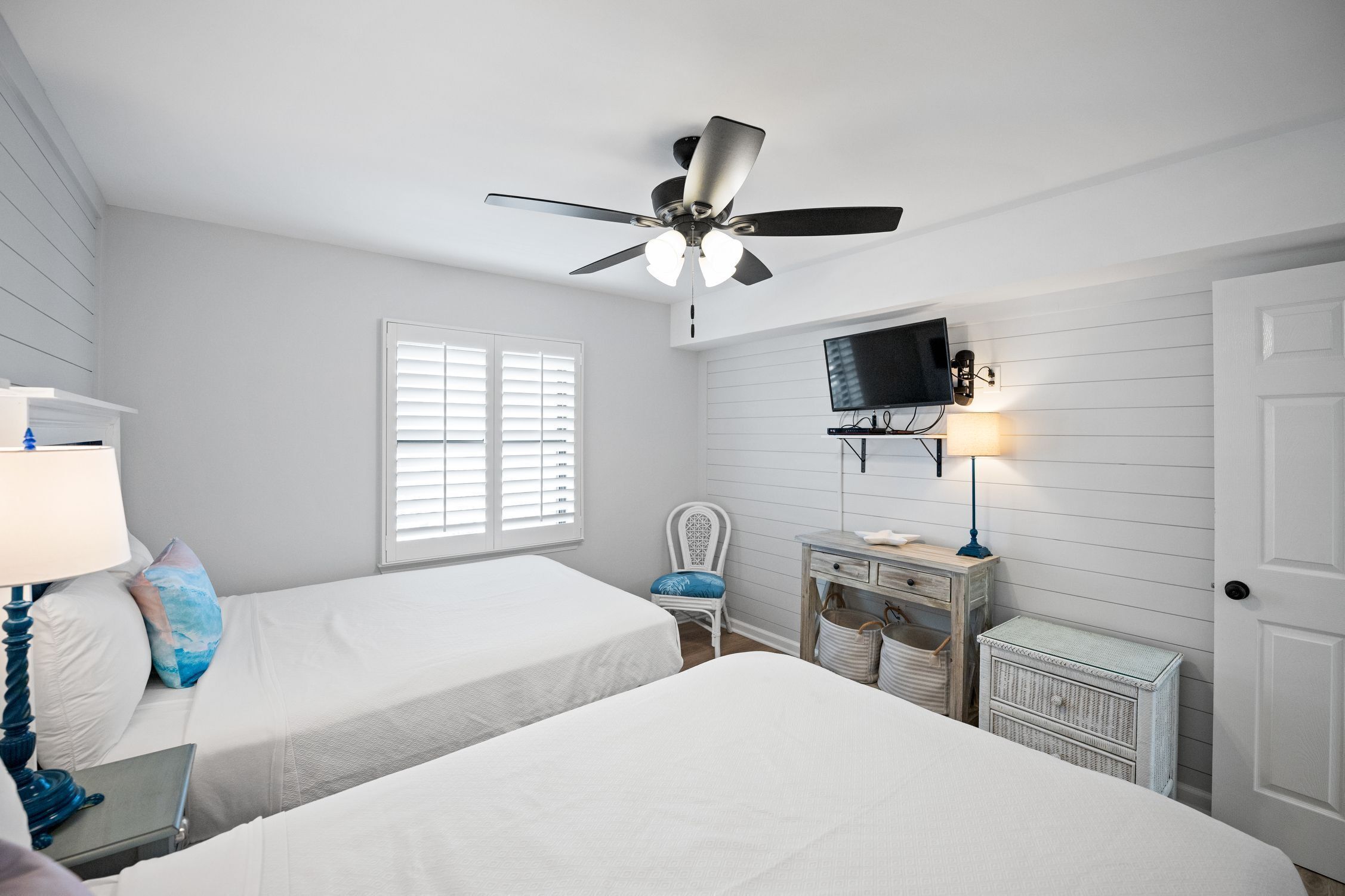 Ein Schlafzimmer mit zwei Betten, einem Deckenventilator, einem Fernseher und einem Schreibtisch mit Lampe.