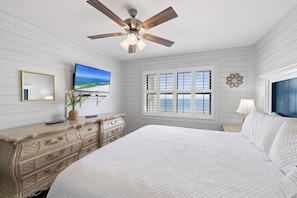 A bedroom with a bed, a dresser, a ceiling fan, a TV, and a window with shutters. - Sunswept 701 by Liquid Life (Orange Beach)