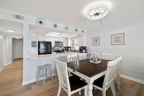 A modern kitchen with white cabinetry, a black refrigerator, and a dining area with a wooden table and white chairs. - Sunswept 701 by Liquid Life (Orange Beach)