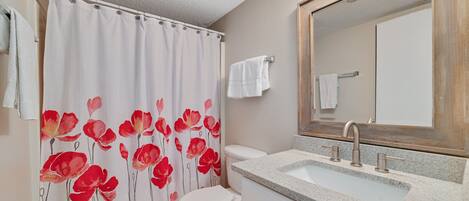 Een badkamer met douchegordijn met bloemenprint, toilet, wastafel met spiegel erboven en een handdoekrek.