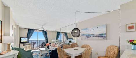 A modern living room with a dining area, a balcony with a view, and a ceiling fan.