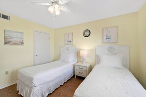 Une chambre avec deux lits, un ventilateur de plafond, une horloge et des œuvres d’art accrochées aux murs.