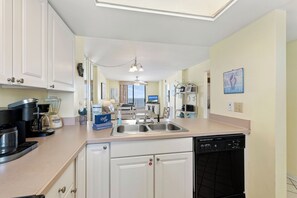 Une cuisine moderne avec des meubles blancs, une machine à café, un lave-vaisselle et une vue sur le salon.