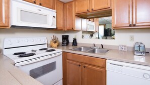 A kitchen with wooden cabinets, a white stove, a microwave, a coffee maker, a toaster, and a dishwasher. - Sunswept 704 by Liquid Life (Orange Beach)