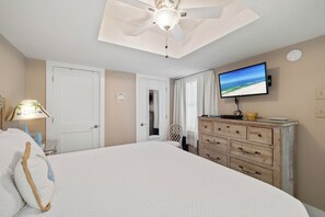 Une chambre à coucher comprenant un lit, une commode, un téléviseur fixé au mur et un ventilateur de plafond.