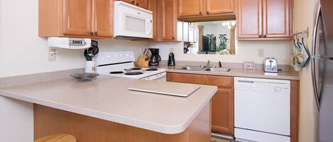 A kitchen with wooden cabinets, a microwave, a stove, a sink, and a dishwasher. There are two wooden stools at the island.