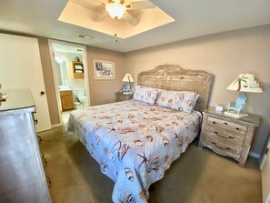 Ein Schlafzimmer mit einem Bett, zwei Nachttischen, einem Deckenventilator, einer Tür zu einem Badezimmer und einem kleinen Tisch mit einer Lampe.