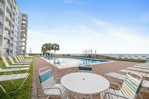 A pool area with lounge chairs and a table, surrounded by a building with balconies. - Sunswept 704 by Liquid Life (Orange Beach)