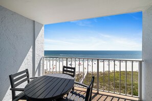 Een balkon met een tafel en stoelen, met uitzicht op een strand met parasols en mensen.