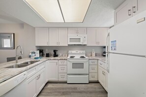 Una cocina moderna con armarios blancos, un microondas integrado, una estufa y un refrigerador.