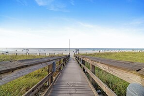 Ein hölzerner Steg führt zu einem Strand unter blauem Himmel.