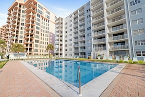 Un edificio de apartamentos moderno con piscina, varios balcones y un camino de ladrillo.
