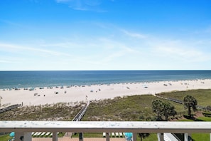 Ein Strand mit freiem Blick auf das Meer, einem eingezäunten Weg und einer begrünte Fläche mit Bäumen.