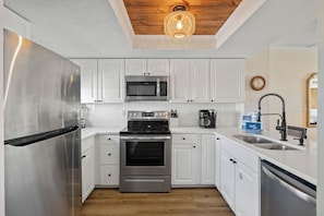 Una cocina moderna con electrodomésticos de acero inoxidable, armarios blancos y techo de madera.
