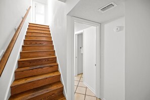 Un escalier en bois mène à une pièce aux murs blancs et au sol carrelé.