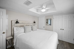 A bedroom with a bed, two bedside lamps, a ceiling fan, a white door, and a mirror on the wall. - Sunswept 801A by Liquid Life (Orange Beach)
