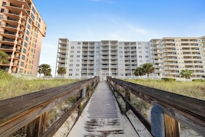 A wooden boardwalk leading to a beachfront residential area with multi-story buildings. - Sunswept 801A by Liquid Life (Orange Beach)