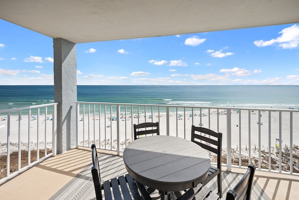 A balcony with a table and chairs overlooking a beach with people and umbrellas. - Sunswept 801A by Liquid Life (Orange Beach)