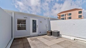 Un immeuble résidentiel à la façade blanche, doté d’une porte et de deux unités de climatisation situées au rez-de-chaussée.