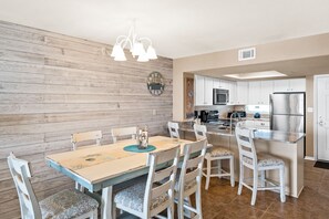 Una cocina con armarios blancos, un refrigerador de acero inoxidable y un comedor con mesa y sillas de madera.