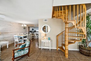A modern interior with a dining area, a staircase, and a kitchen in the background. - Sunswept 806 Penthouse by Liquid Life (Orange Beach)