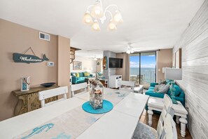 A spacious living room with a large window, a dining area with a view, and a cozy seating area. - Sunswept 806 Penthouse by Liquid Life (Orange Beach)