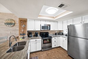 A modern kitchen with white cabinets, stainless steel appliances, a built-in microwave, and a large refrigerator. - Sunswept 806 Penthouse by Liquid Life (Orange Beach)