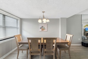 A dining room with a wooden table and chairs, a ceiling light fixture, and a wall-mounted picture. - Sunswept 807 Penthouse by Liquid Life (Orange Beach)